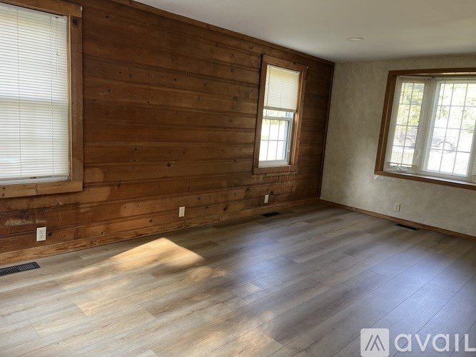 A room with wooden walls and floors and two windows.
