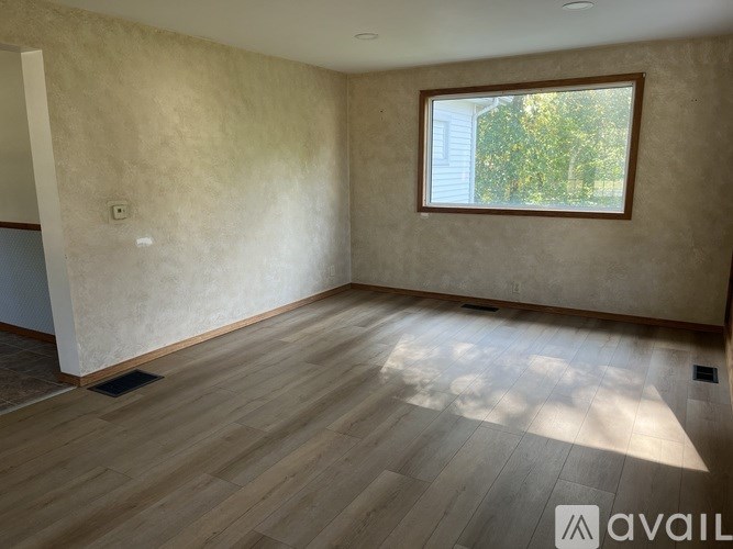 A room with wooden flooring and a window showing trees outside.