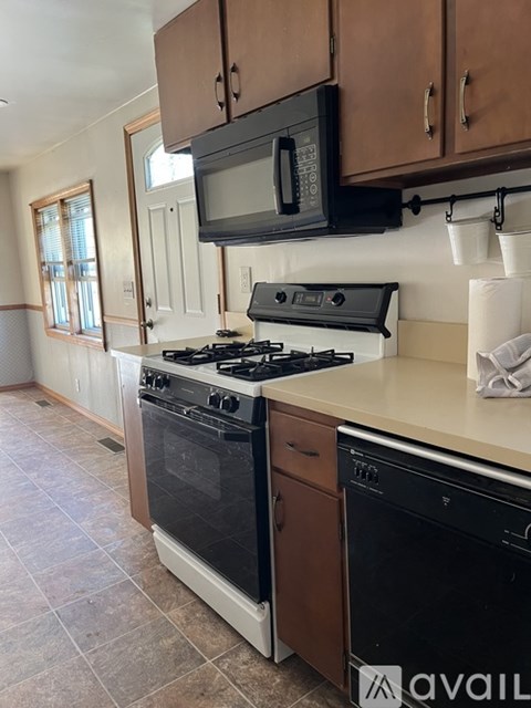A room with a carpeted floor and a white door that opens to a kitchen area.