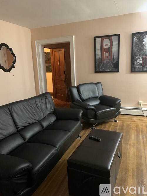 A living room with black leather furniture and a wooden floor.