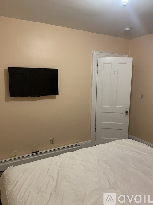 A bedroom with a bed, a door, and a flat screen TV mounted on the wall.