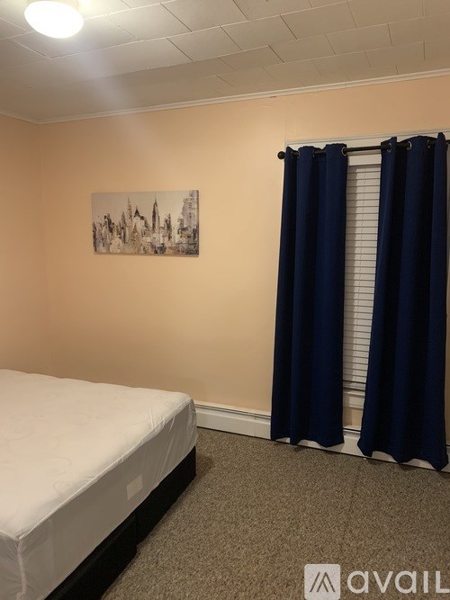 A bedroom with a bed, a window with blue curtains, and a picture on the wall.
