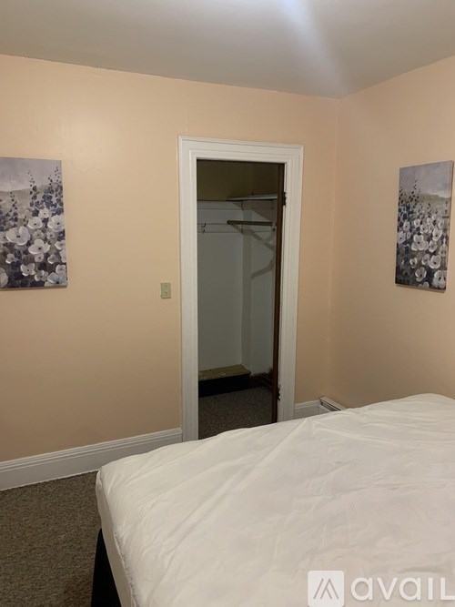 A bedroom with a bed, two pictures on the wall, and a door leading to a hallway.