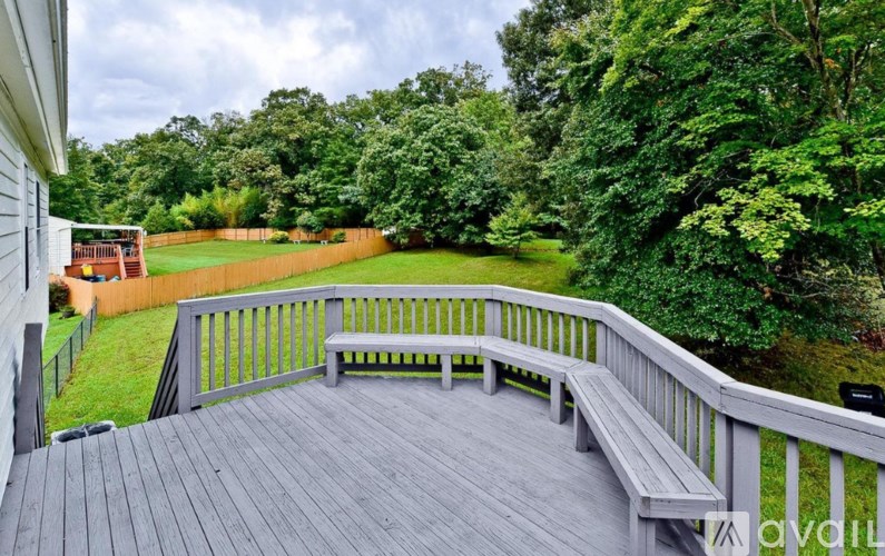A wooden deck with a bench overlooks a lush green yard.