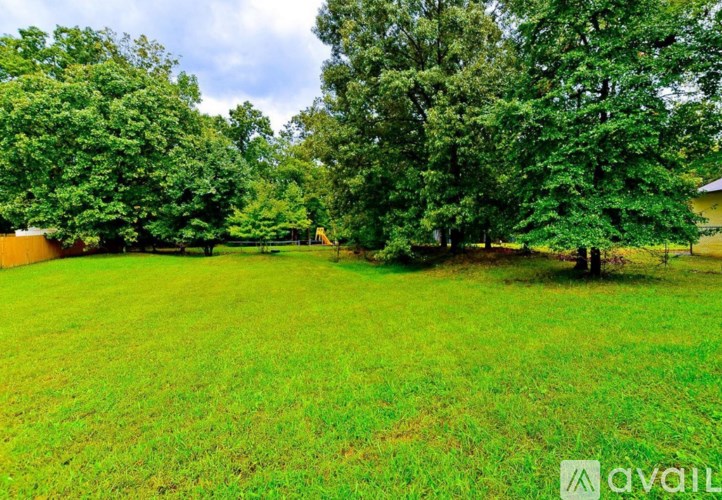 A grassy field with trees and a building in the background.