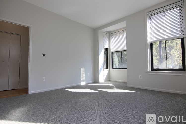 A spacious room with a carpeted floor and a large window with blinds.