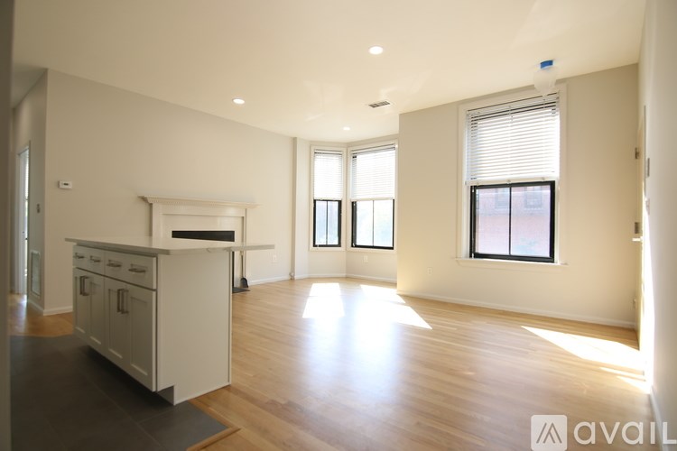 A spacious, empty room with wooden floors and a kitchen area with white appliances.