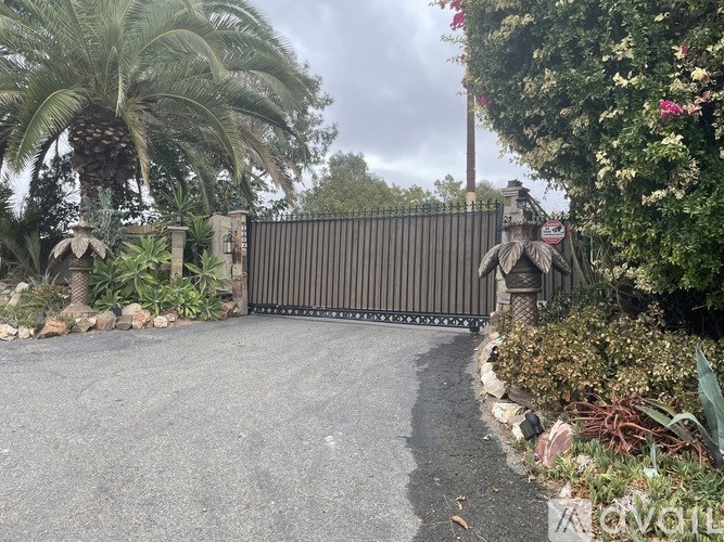 A black gate with a decorative top is in the middle of a driveway.
