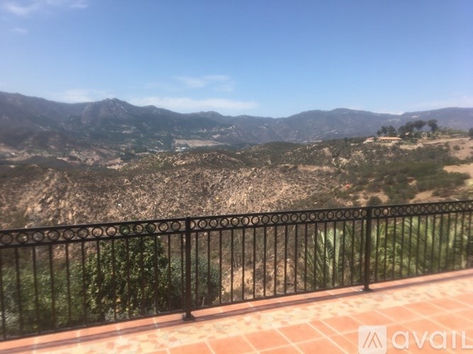 A balcony with a black railing overlooks a valley with mountains in the distance.