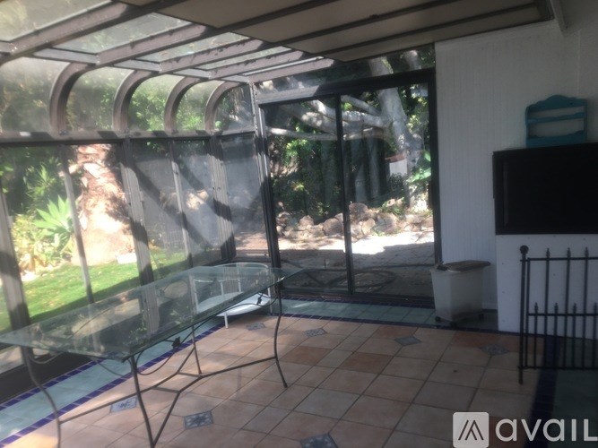 A glass table is in a sunny room with a TV on the wall.