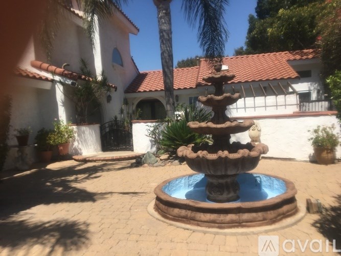 A fountain in the middle of a courtyard with a house in the background.