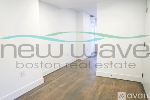 A room with wooden flooring and white walls, with a logo that reads "new wave boston real estate available".