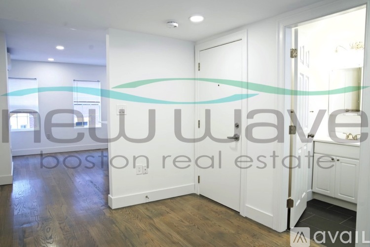 A room with a wooden floor and white walls, with a sign that reads "New Wave Boston real estate available".