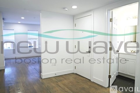 A room with a wooden floor and white walls, with a sign that reads "New Wave Boston real estate available".