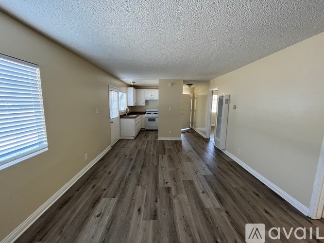 A room with wooden flooring and a kitchen area in the background.