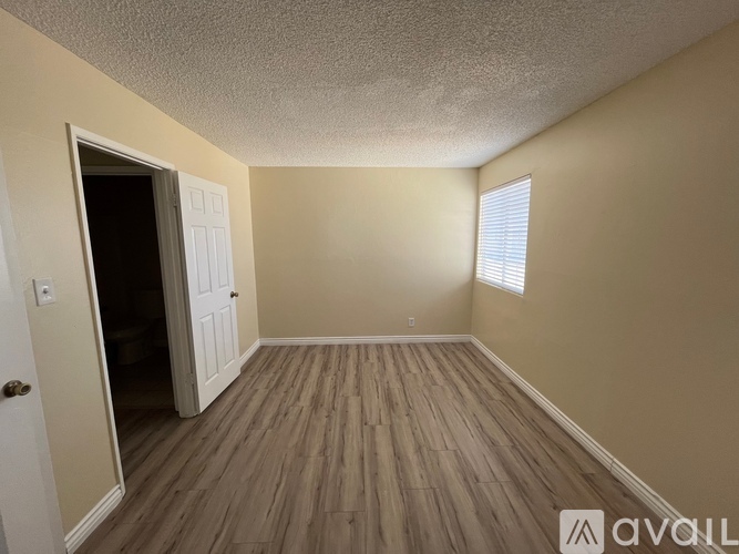 A room with wooden flooring and a door leading to a darker room.