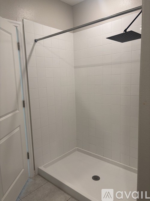 A white tiled shower with a black shower head.