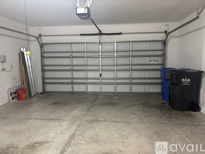 A large garage with a closed white door and a black trash bin.