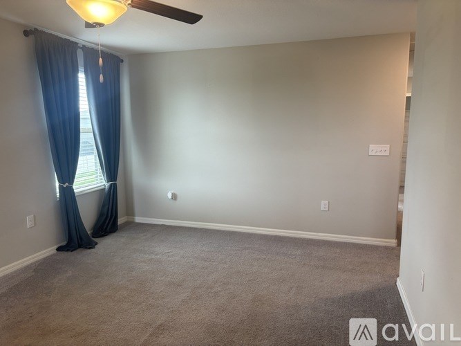A room with a ceiling fan and a window with blue curtains.