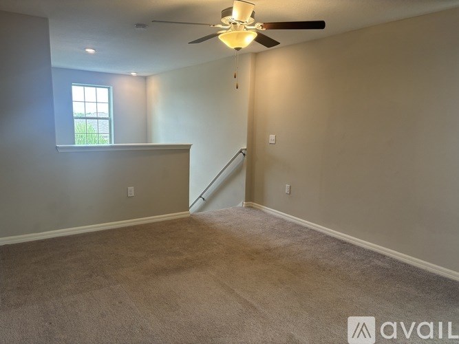 A room with a carpeted floor, a ceiling fan, and a window.