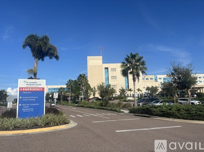 The image shows a hospital entrance with a signboard and a palm tree.