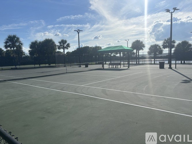 A tennis court with a green roofed pavilion and a fence in the background.