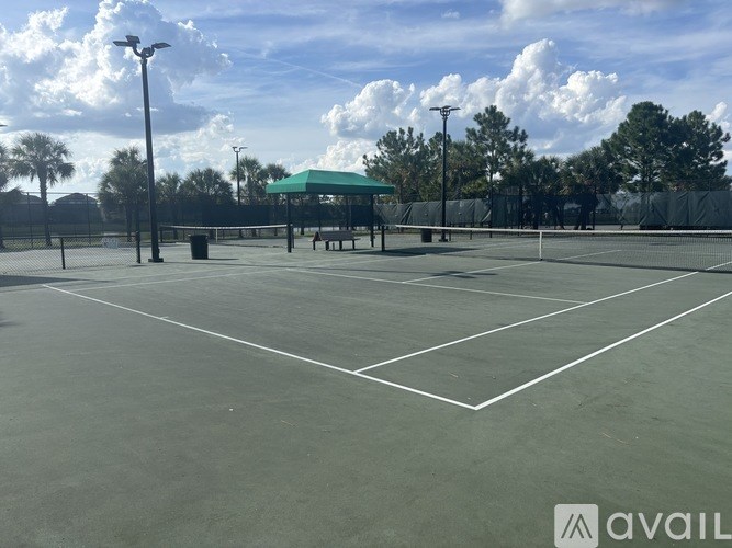 A tennis court with a green roofed shelter and a trash can.