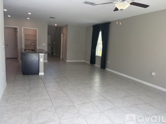 A spacious room with a ceiling fan and a kitchen area with a refrigerator.