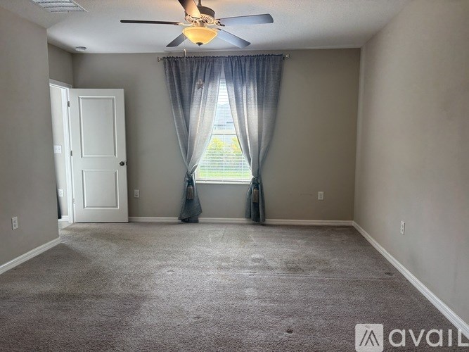A room with a carpeted floor, a ceiling fan, and a window with curtains.