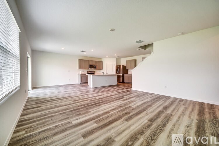 A spacious room with wooden flooring and a kitchen area in the background.