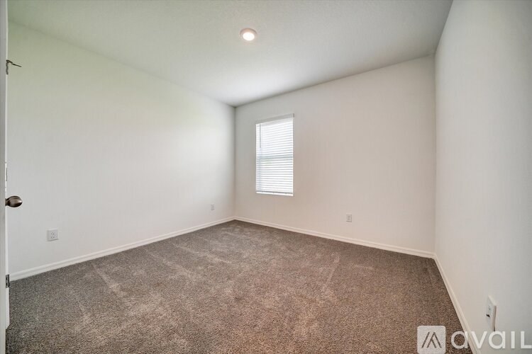 A room with a carpeted floor and a window with blinds.