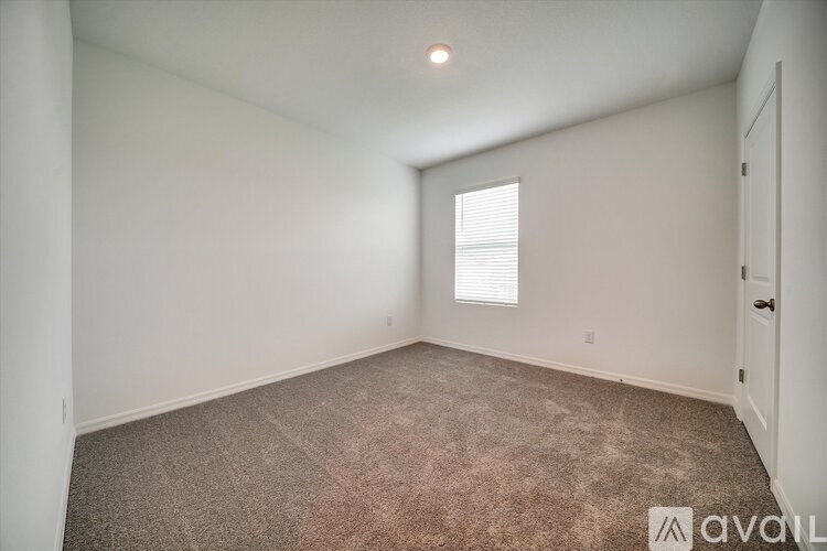 A room with carpeted floor and a window with blinds.