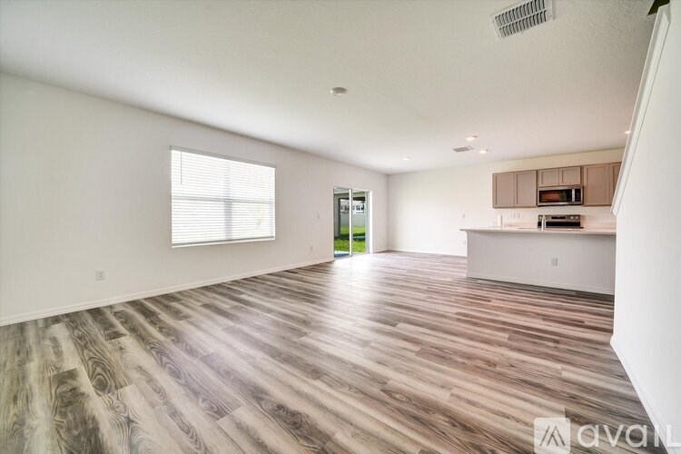 A spacious room with wooden flooring and a window with blinds.