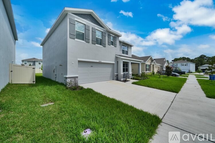 A modern house with a grey exterior and a white garage door is surrounded by a well-maintained lawn and a clear sky.