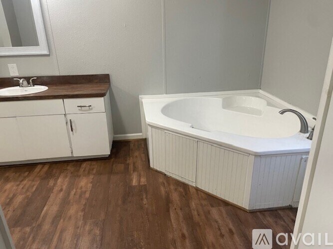 A white bathtub is in a bathroom with wood flooring and white cabinets.