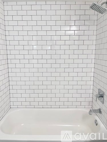 A white tiled bathroom with a white bathtub and a shower head.
