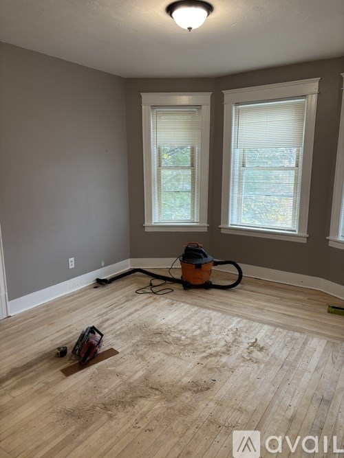 A room with wooden flooring and two windows.