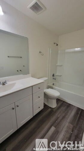 A white bathroom with wood flooring and a toilet.