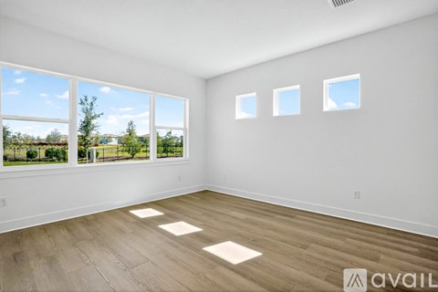 A room with white walls and wooden flooring, with large windows and a view of the outdoors.
