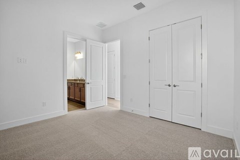 A room with white walls and carpeted floor with a doorway leading to another room.