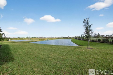 A grassy field with a lake and a tree in the distance.