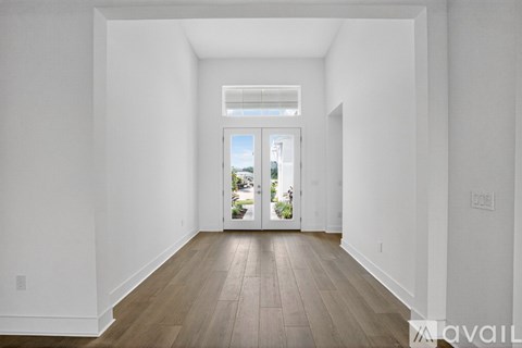 A room with white walls and wooden flooring with a view of the outside through a glass door.