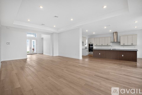 A spacious room with wooden flooring and a kitchen area in the background.