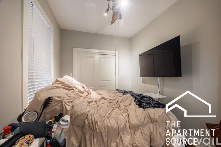 A messy bedroom with a bed covered in blankets and clothes.