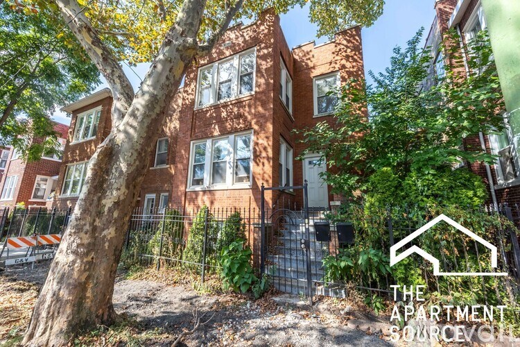 A tree in front of a brick building with a sign that says "The Apartment Source".