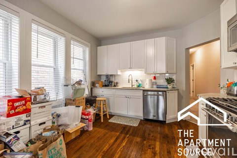 A kitchen with white cabinets and a lot of boxes on the floor.
