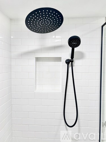A black shower head and hose in a white tiled shower.