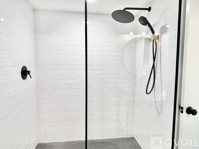 A white tiled shower with a black shower head and hose.