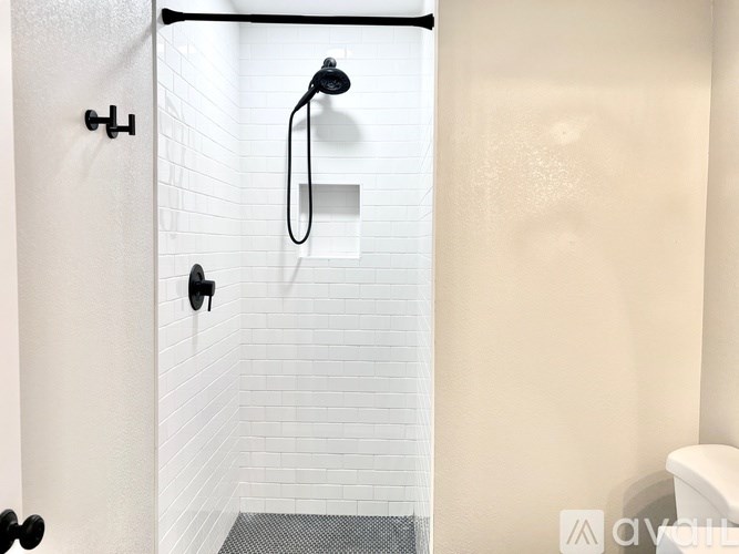 A white tiled shower with a black shower head and hand held shower.