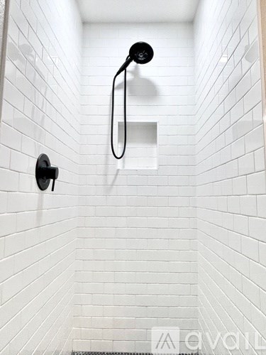 A white tiled shower with a black shower head and hand held shower.